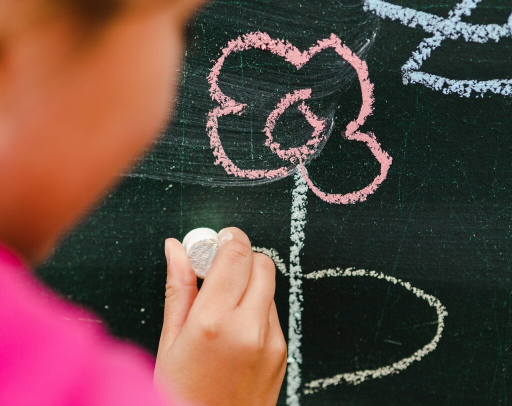 Kind malt eine Blume mit Kreide an die Tafel